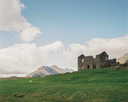 Abandoned house with green grass field and mountains in the background