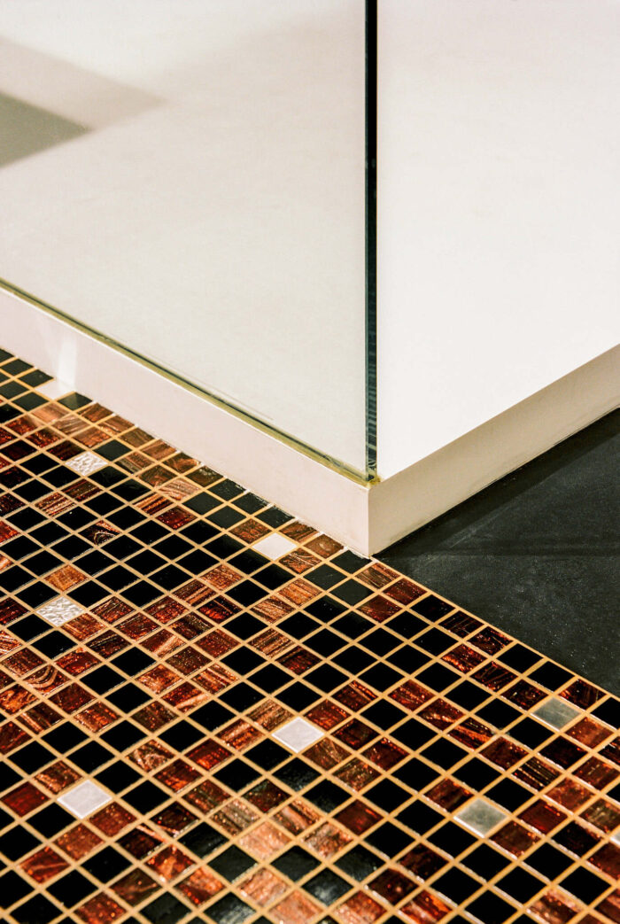 Bathroom detail of floor with black brown and golden tiles and white shower